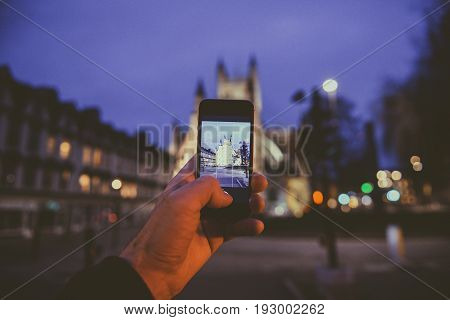 BATH, UNITED KINGDOM - MARCH 8, 2017: Point of view of man taking photograph with the mobile phone smartphone of the illuminated cathedral Bath Abbey in Bath United Kingdom