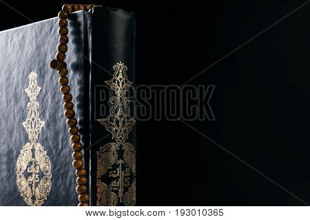 Close-up of Islam holy book of Muslims the Quran/ Koran with prayer rosary beads isolated on black background with copy space.