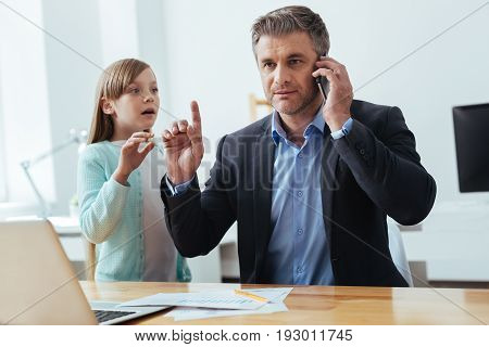 Wait a minute. Sociable ambitious hardworking businessman taking a phone call and discussing business issues while his child asking for attention