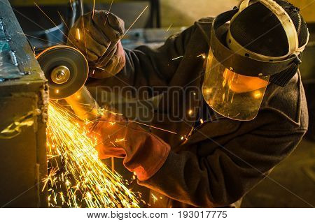 A man in working form and a face mask cuts a metal saw with a Bulgarian on the background of a metallurgical industrial plant.