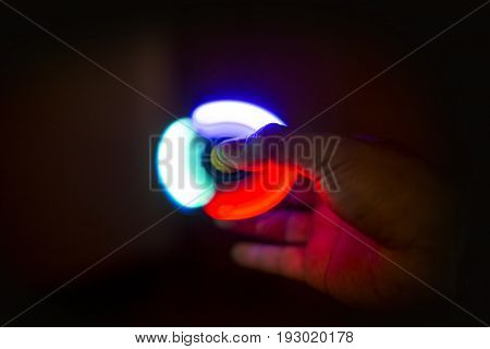 Play Fidget spinner spinning and Hand on dark background With Ligtht