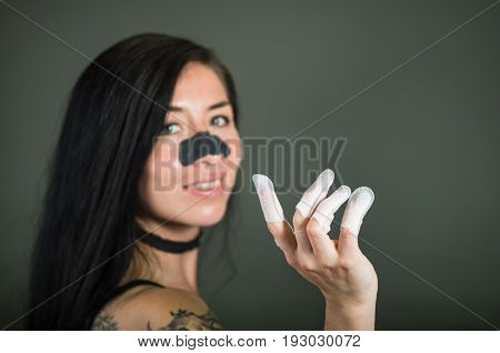 Close up of young woman wearing nails protector in her nails and a nose mask to clean skin from black spots, in a black background.