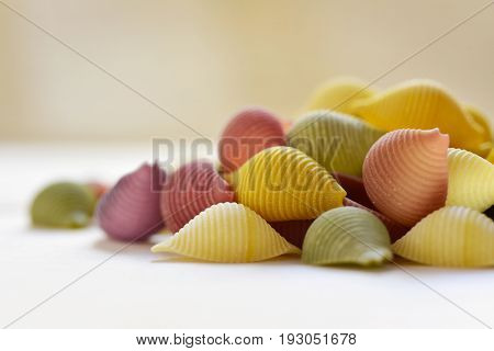 closeup of a pile of uncooked conchiglie, italian seashell pasta, with different colors: yellow as usual, red made with tomato and green made with spinach