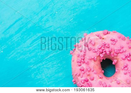 Pink glazed doughnut with sugar sprinkles in right bottom corner on light blue background copyspace template birthday card poster top view macro