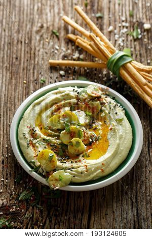 Broad bean hummus, with addition of olive oil, paprika powder, fresh mint and sesame seeds,  delicious and healthy vegan dip or spread, on a wooden rustic table, top view