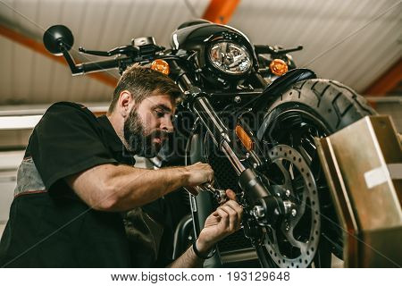 A professional mechanic unscrews the front wheel of a motorcycle. Bike is on the lift at the service station.