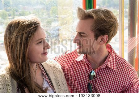 Young couple in traditional Bavarian costume in love inside a ferris wheel on Munich Oktoberfest