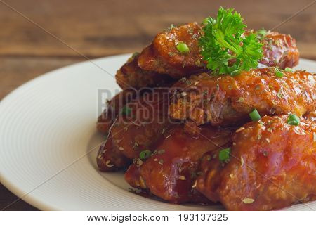 Barbecue chicken wings on white plate in close up view. Homemade barbecue chicken wing delicious moist and spicy. Deep fried chicken with barbecue sauce decorated with spice and parsley ready to served.