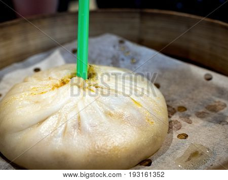 Large Chinese steam bun (xiaolongbao), a bread-like food with hot soup inside. A straw is used to drink the soup first. Bun is presented on a bamboo steamer.