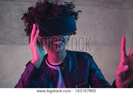 oung stylish girl wearing VR glasses and gesturing on concretewall.