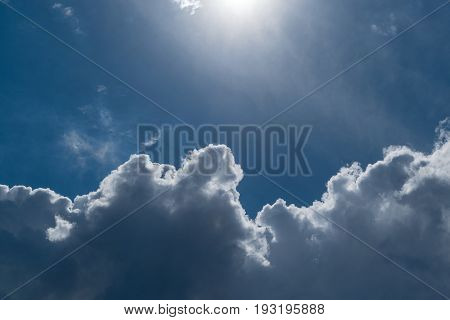 Blue sky with Cumulus clouds. Top the sun shines. The bright sun illuminates Cumulus clouds. The sky is clear and blue. A small haze.