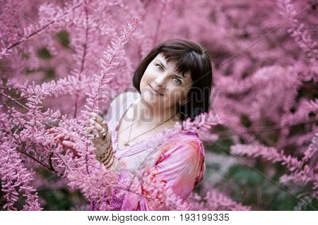 Portrait of a middle-aged woman in pink flowers of tamaricaceae. Beautiful romantic woman in Tamarix