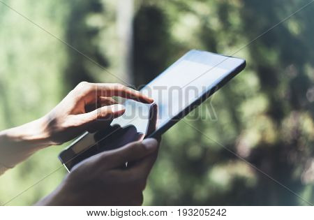 Hipster young girl using tablet or holding gadget planning travel plan. Female hands holding computer tourist traveler texting message on device on green background in Parc Laberint Barcelona. Mockup for text flare and bokeh
