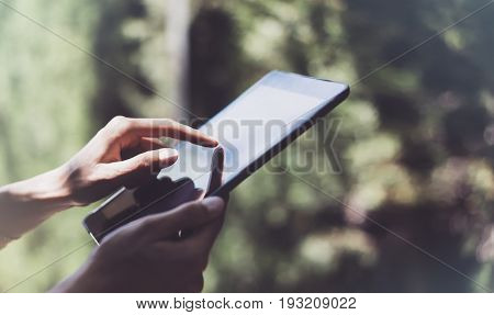 Hipster young girl using tablet or holding gadget planning travel plan. Female hands holding computer tourist traveler texting message on device on green background in Parc Laberint Barcelona. Mockup