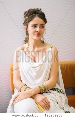 portrait of a young beautiful sharming greek woman in ancient white dress sitting on a sofa
