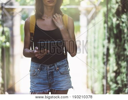 Hipster young girl with bright backpack and vintage camera using tablet or holding gadget planning travel plan. View tourist traveler on background Parc Laberint Barcelona. Mock up for text message