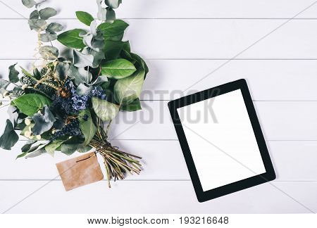 Closeup tablet with a empty blank screen monitor with a bouquet of flowers on white table background with natural wood vintage planks wooden texture top view horizontal digital computer with blank template copy space screen for your information or content