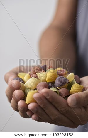 young man with a pile of uncooked conchiglie, italian seashell pasta, with different colors: yellow as usual, red made with tomato and green made with spinach