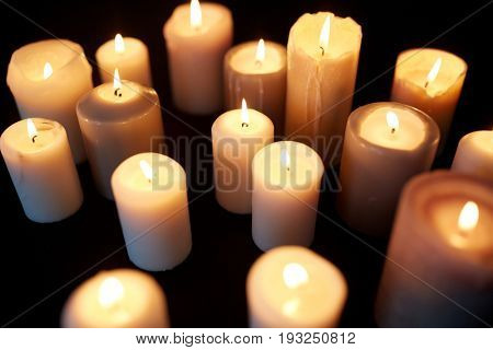 mourning and commemoration concept - candles burning in darkness over black background