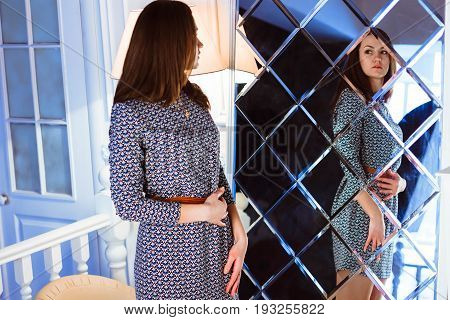Fashion and shopping. Woman trying dress sweater choosing clothing. Attractive female shopper looking in mirror standing in clothes store.