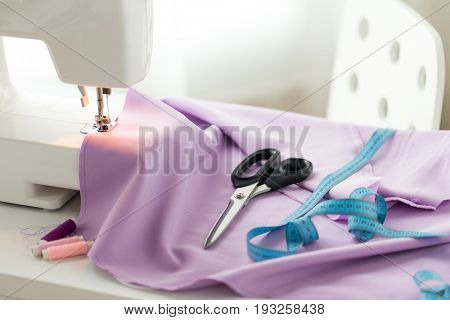 needlework, technology and tailoring concept - sewing machine with scissors, buttons, tape measure and fabric