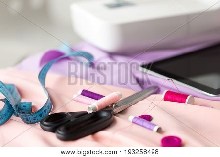 needlework, technology and tailoring concept - sewing machine with scissors, buttons, tape measure and fabric