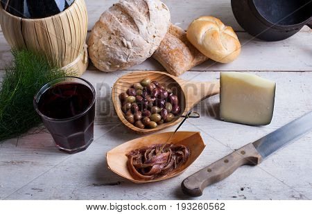 Italian slow food on the white table. Olives cheese bread anchovies and red wine