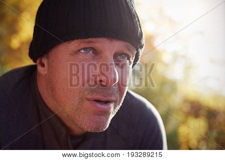 Mature Male Runner Pausing For Breath During Exercise In Woods