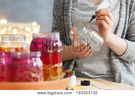 Young woman decorating DIY jars with paint