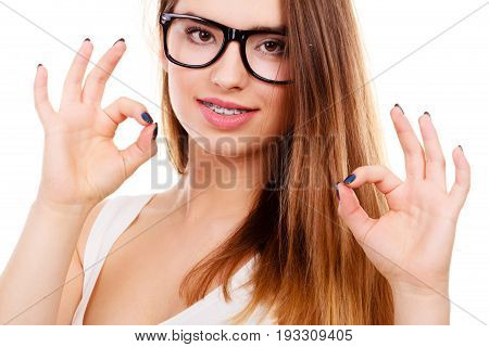Vision and dentistry problems concept. Happy nerdy teenage wearing big eyeglasses showing her braces on teeth a ok gesture.