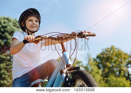Moving forward. Clever attentive charismatic child enjoying an active hobby while riding a bicycle and wearing special helmet