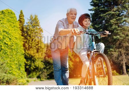 Inspiring grandparent. Admirable quick witted aged gentleman encouraging his child riding a bike and looking after him while he learning how doing it