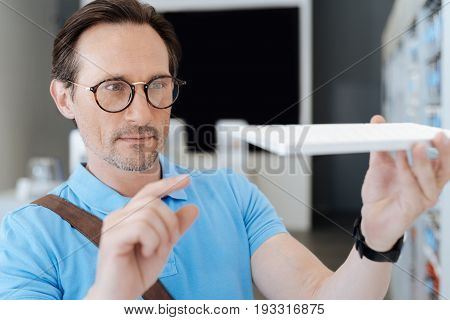 Just look at the quality of it. Focus male customer wearing glasses holding a keyboard and keeping his eyes peeled while shopping at an electronics store.