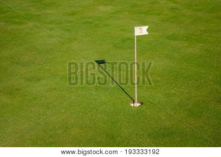 Glof flag mark in hole throwing shadow on the green course grass, golf playing concept