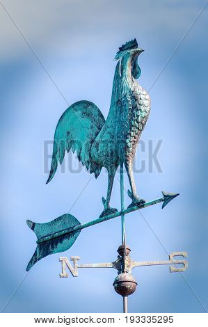 Big on a weathervane. Metal Weathercock pointing south west. Blue green weather vane showing wind direction.
