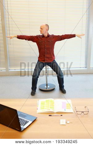 middle age man stretching arms, relaxing neck - short break for exercise on pneumatic stool in office