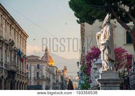 Statue outside the Church of St. Agatha in Catania Sicily with the town and Mount Etna in the background