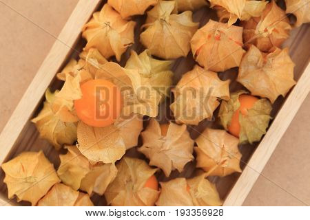 Cape gooseberry fruits in wooden box brown autumn crops background top view.