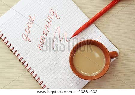 Cup of fresh coffee on the notebook sheet with the words good morning