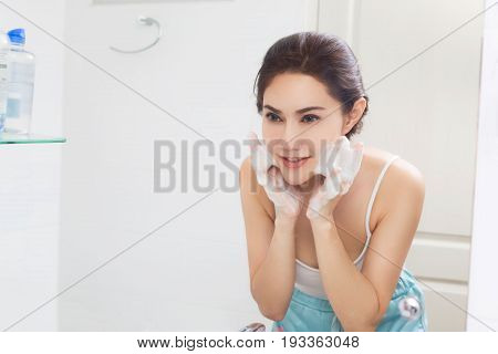 Woman happy cleanses the skin with foam in bathroom.