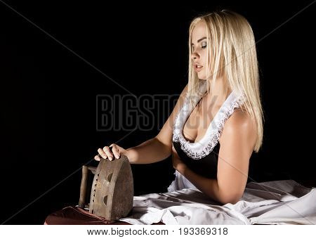sexy blonde woman in housekeeper suit, ironing white shirt with old iron. retro style. housewife concept