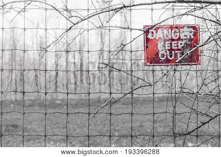 Red Danger Sign Posted To Barbed Fence Tangled In Branches, Warning People To Keep Out