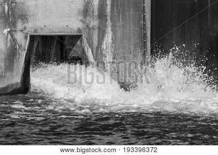 Water splashing and pouring out from a dam overflow concrete culvert black and white image with frozen motion