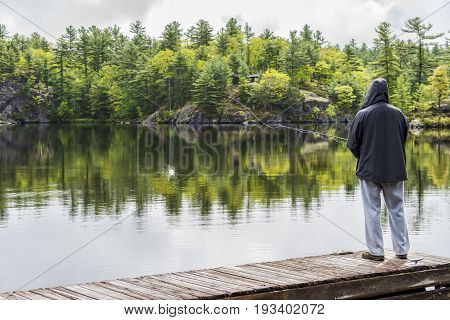 Man Fishing Off Dock, Line Landing In Water With Small Splash As He Casts