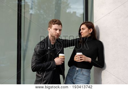 People relationships and modern urban lifestyle concept. Isolated shot of handsome young man with stubble talking to pretty girl while drinking takeaway coffee out of papercups on their first date