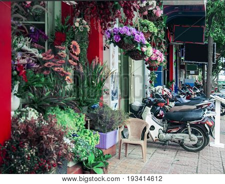 Street in a Vietnamese city next to a flower shop and a lot of parked bikes.