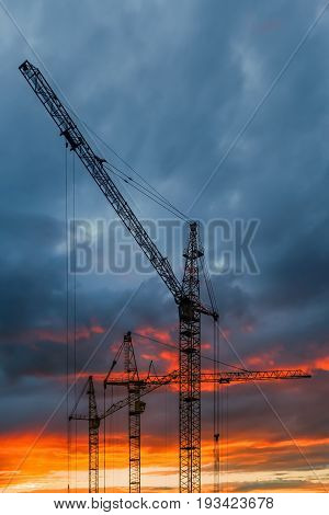 Silhouette of construction cranes on sunset sky background
