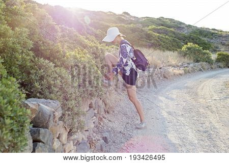 Young woman with white hat tying shoelace, hot summer in Kolokitha island, Crete, Greece
