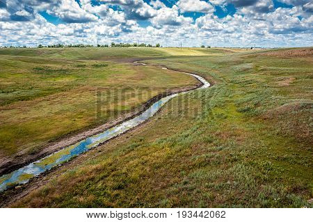 South of Russia spring in the Kalmyk steppes. Brook drying up by the hot Kalmyk summer crossing the ravines against the background of an invasive sky.