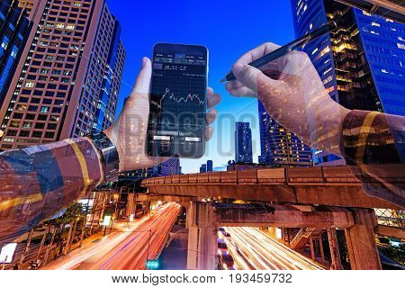 Double exposure of hands in hipster shirts holding smart phone for check stock market graph withlight of night building background Business Trading concept.